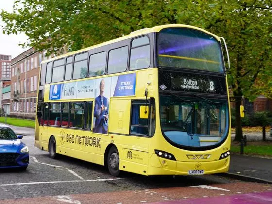 A yellow Bee Network bus waiting at a road crossing.