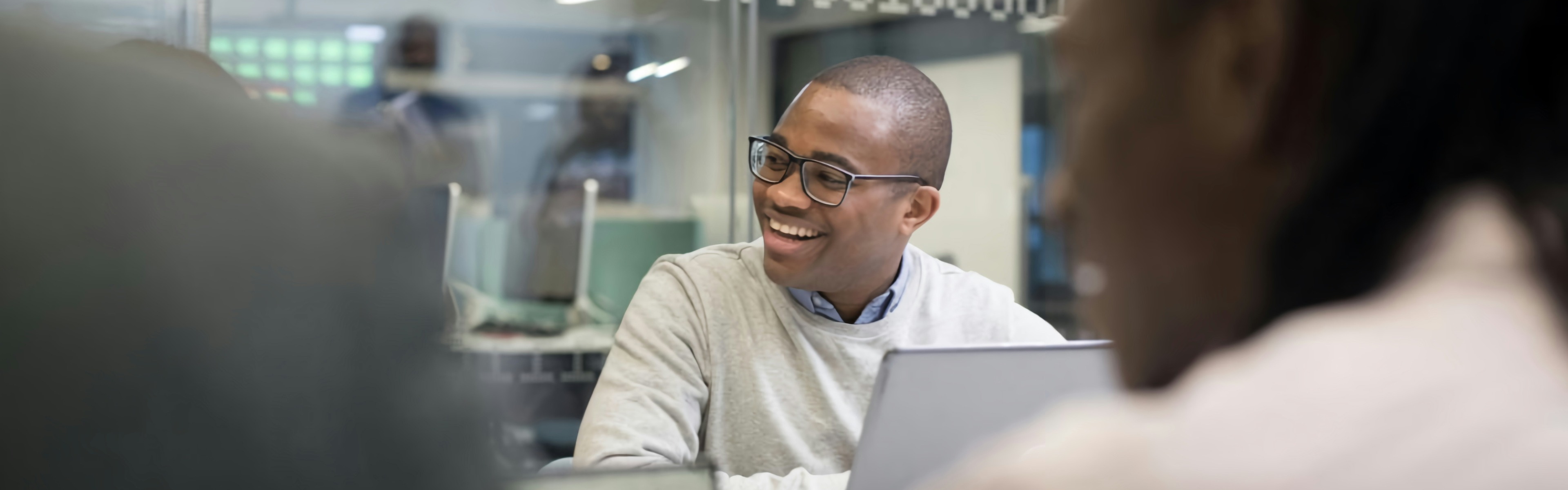 A man with a laptop sat around an office meeting table with colleagues 