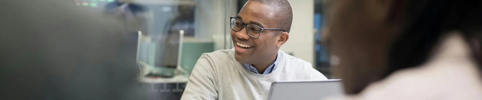 A man with a laptop sat around an office meeting table with colleagues