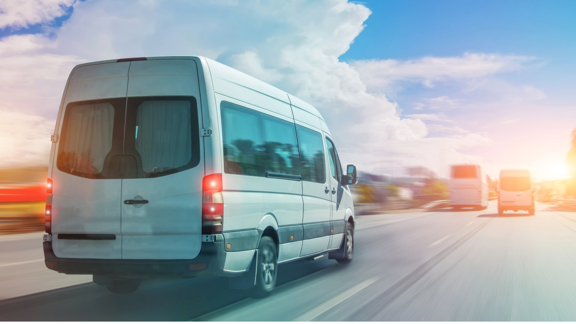 A white mini bus travelling along a road with other traffic.