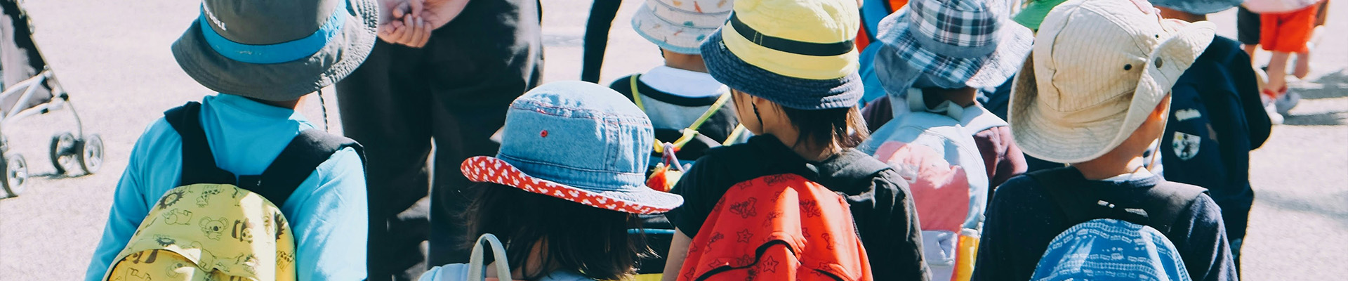 A group of school children with brightly coloured backpacks cross the road together.