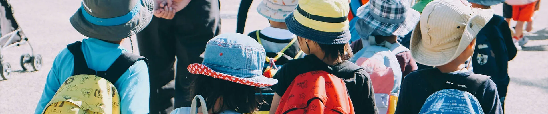 A group of school children with brightly coloured backpacks cross the road together.