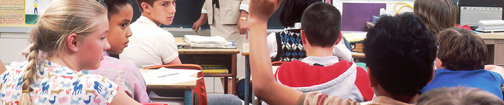 A group of children in a classroom answer the teacher's questions.
